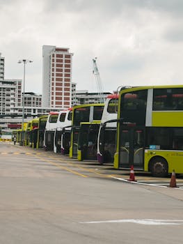 Line of double-decker buses parked at an urban terminal with city buildings in the background.
