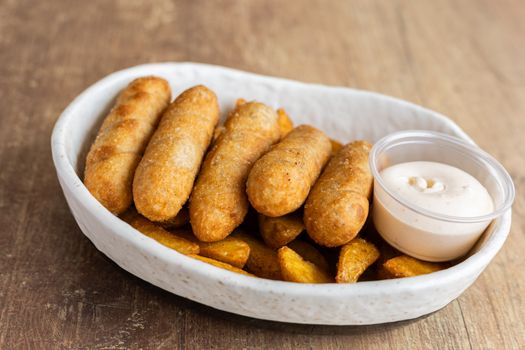 A hearty dish of crispy croquettes served with potato wedges and a creamy dipping sauce.