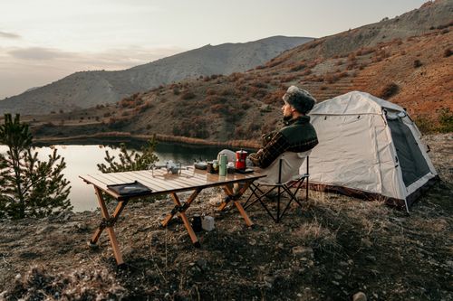 Free Man enjoying a serene camping experience by a picturesque mountain lake during sunset. Stock Photo