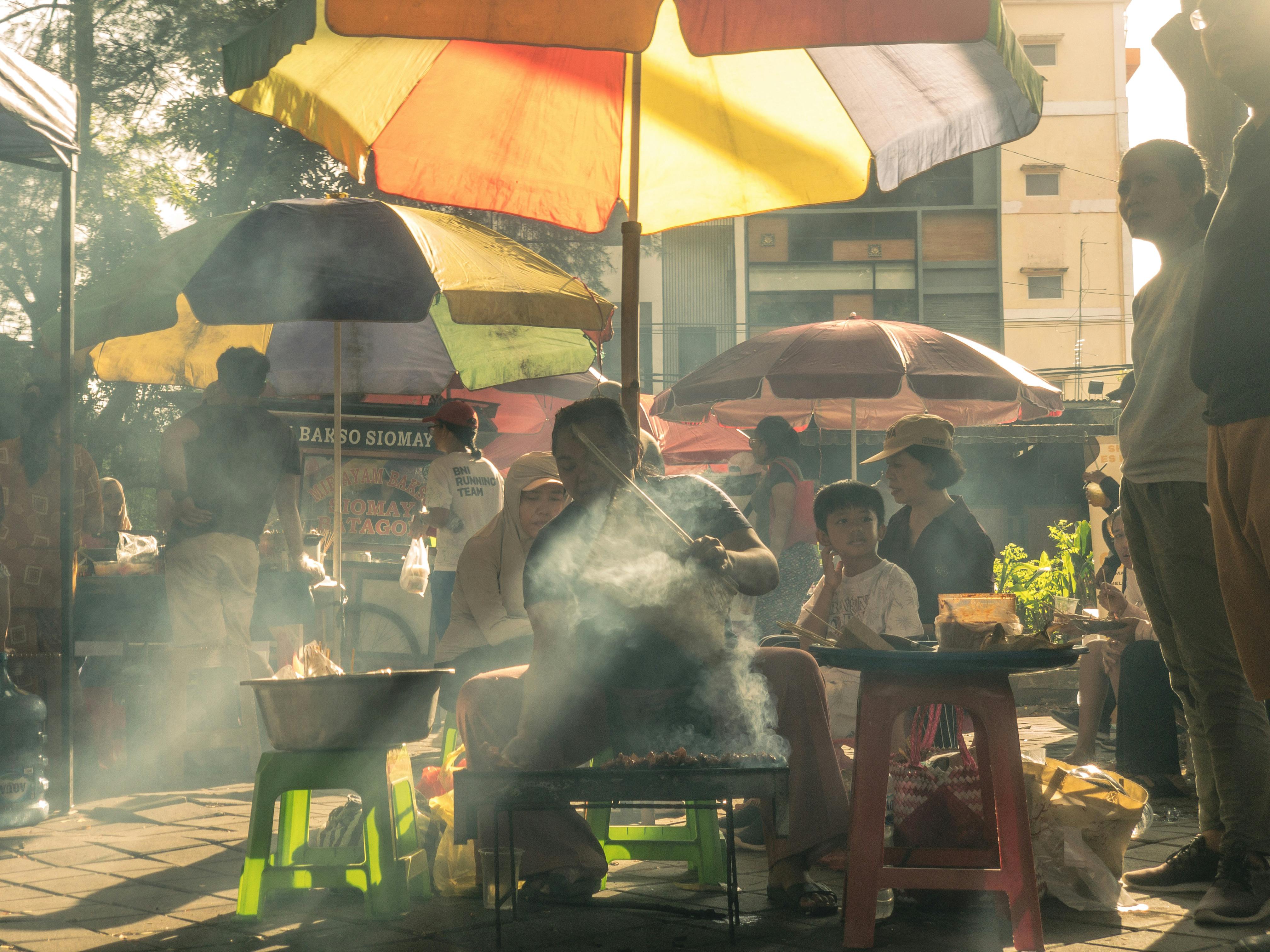 A bustling morning market with locals eating at communal tables, steam rising from food stalls
