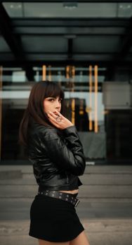 Fashionable woman in a black leather jacket posing outdoors with a confident expression.