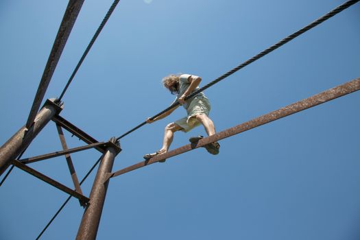 Man balances on a rope at height against clear blue sky, showcasing courage and adventure.