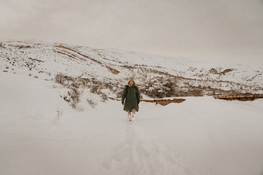 A lone woman wearing a winter coat walks through a snowy mountain landscape.