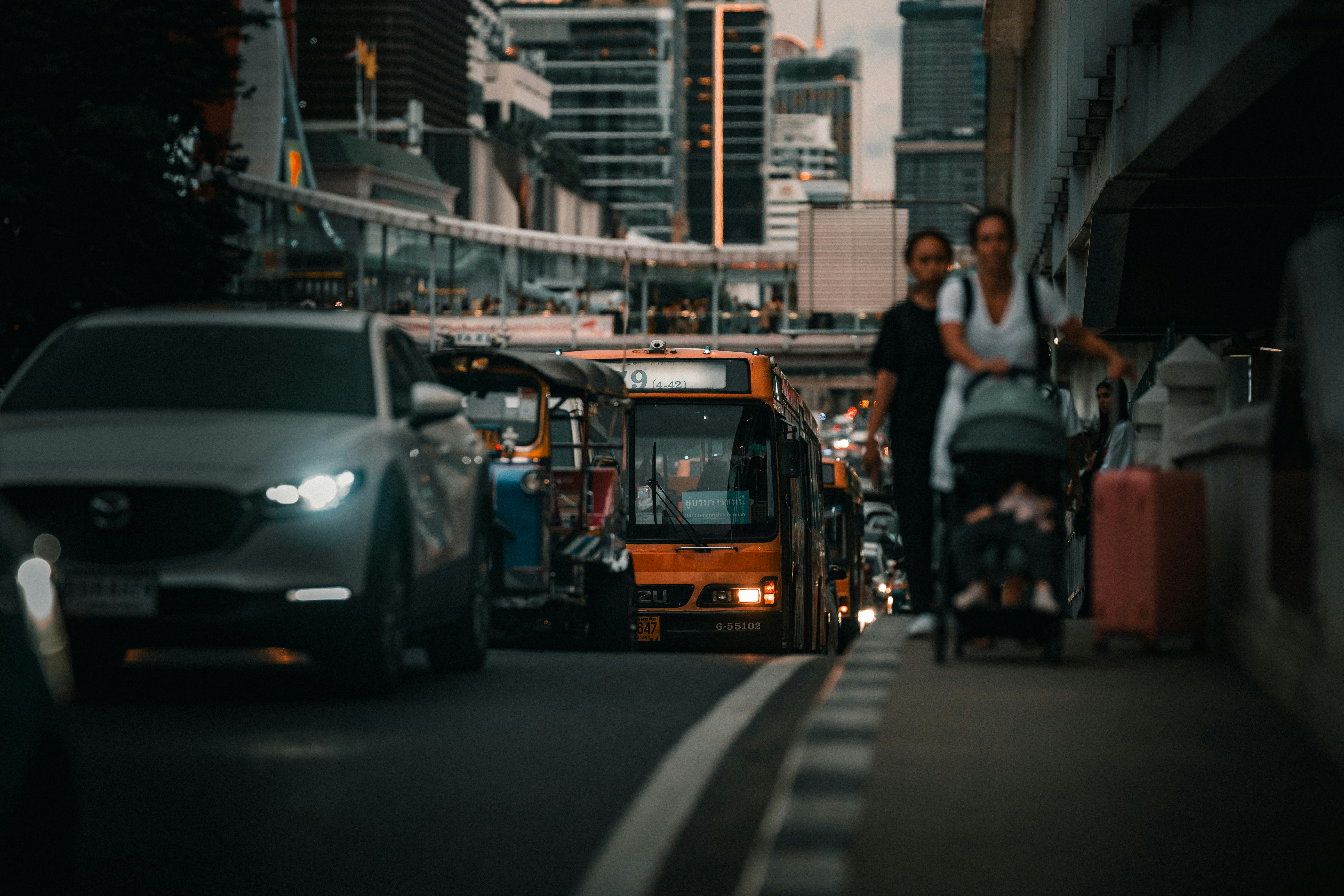 Kostenlos Eine belebte Straße in Bangkok, Thailand, mit Verkehr und Fußgängern in der Abenddämmerung, die das städtische Leben widerspiegelt. Stock-Foto