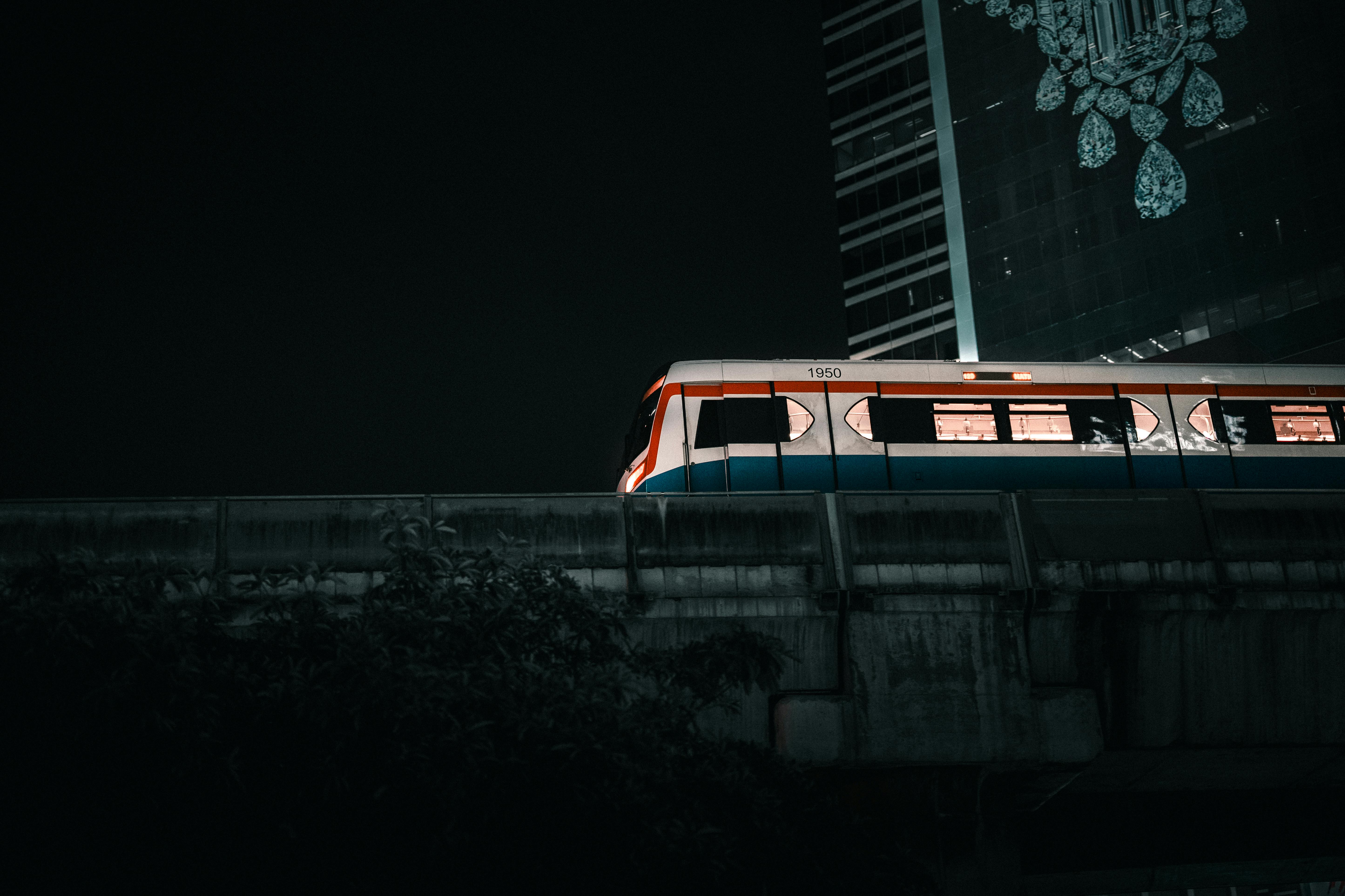 A vibrant urban night scene featuring a Bangkok Skytrain passing by a skyscraper.