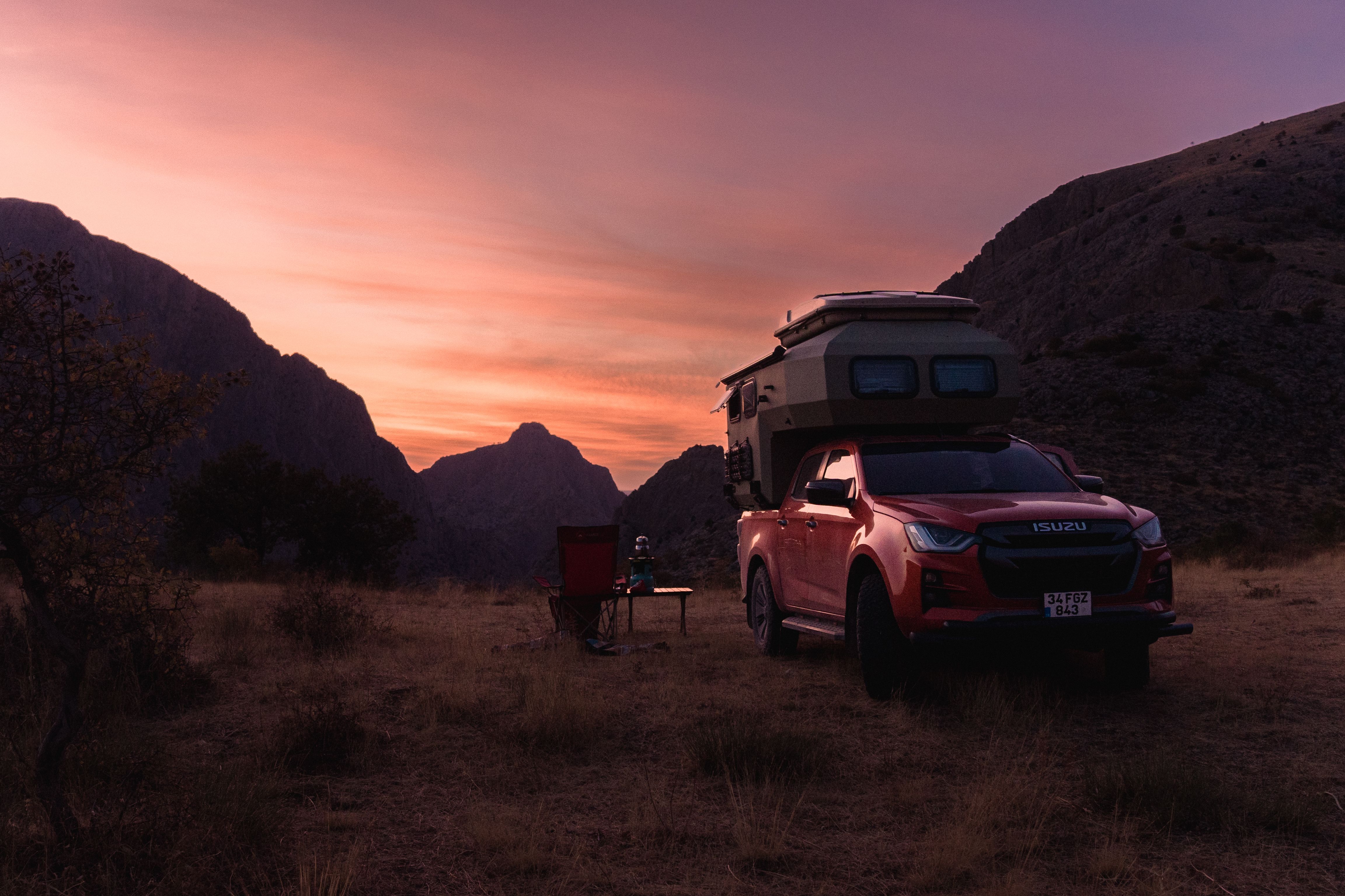 Overland off-road vehicle with camper setup parked in remote mountain terrain at sunset