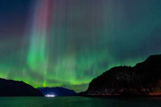 Beautiful display of Northern Lights over a serene mountain and water landscape at night.