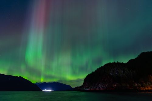 Free Beautiful display of Northern Lights over a serene mountain and water landscape at night. Stock Photo