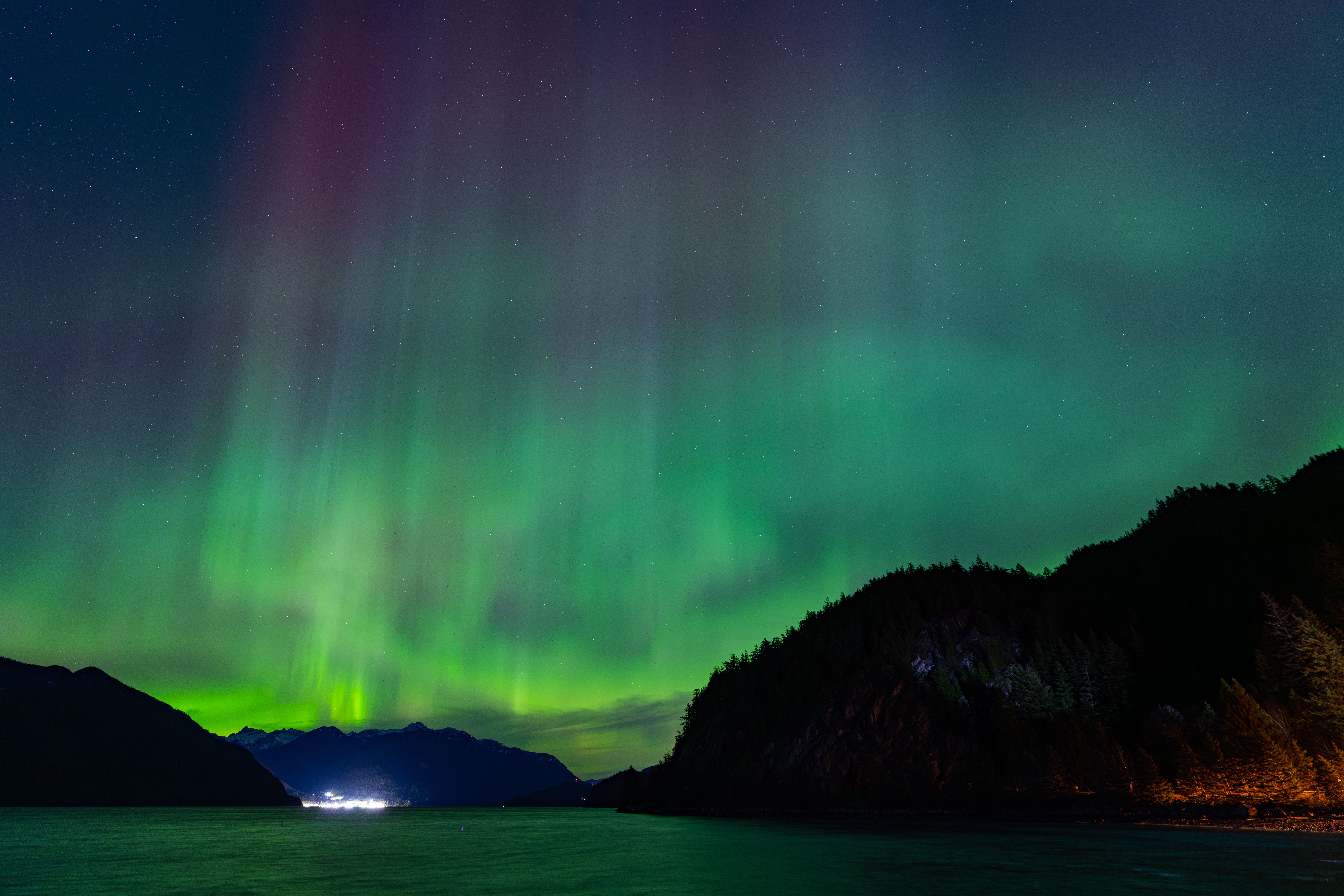 Stunning Northern Lights illuminate the night sky above a serene mountain and lake landscape, creating a magical view.