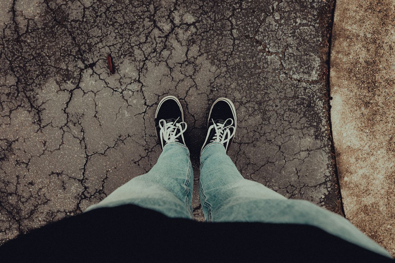 person wearing casual jeans and sneakers standing on cracked pavement
