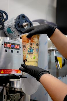 Hands sealing a cup of freshly made boba tea in a cafe, showcasing the process.