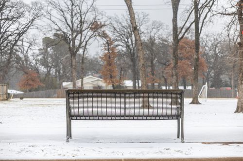 Free A solitary park bench sits quietly amidst a snowy, barren winter park scene. Stock Photo