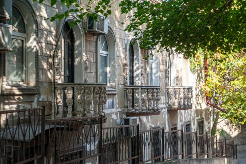 Free Charming historic building facade with elegant arched windows and ornate balconies in dappled sunlight. Stock Photo