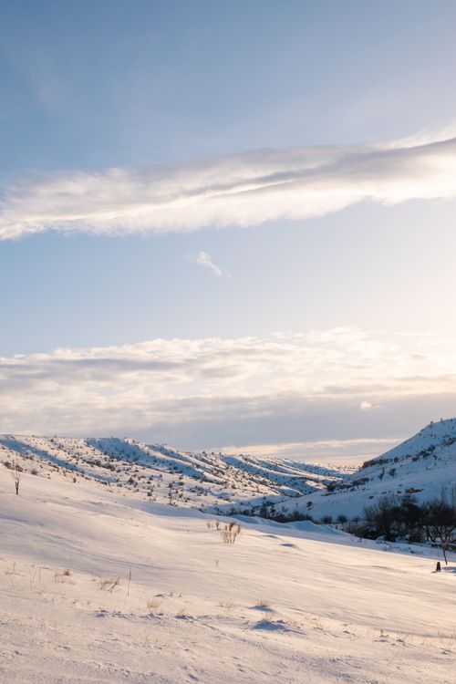 Free Beautiful snowy mountain scene at dawn with soft clouds and bright sky. Stock Photo