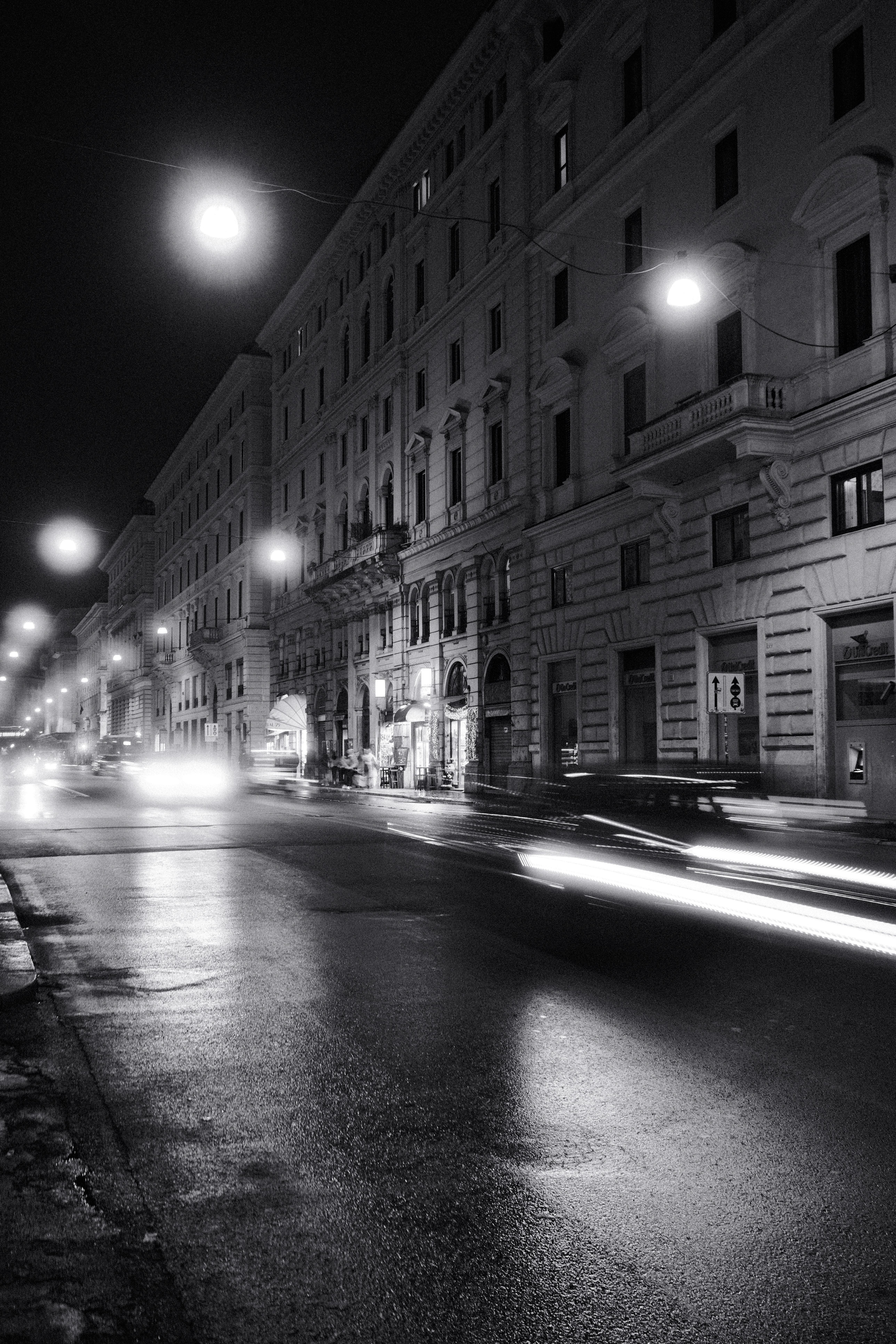 A classic city street scene at night with light trails and vintage architecture, captured in black and white.