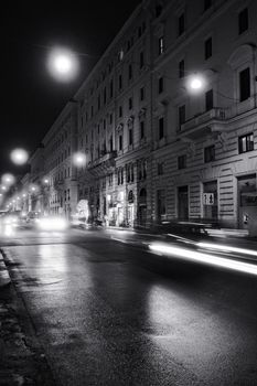 A classic city street scene at night with light trails and vintage architecture, captured in black and white.