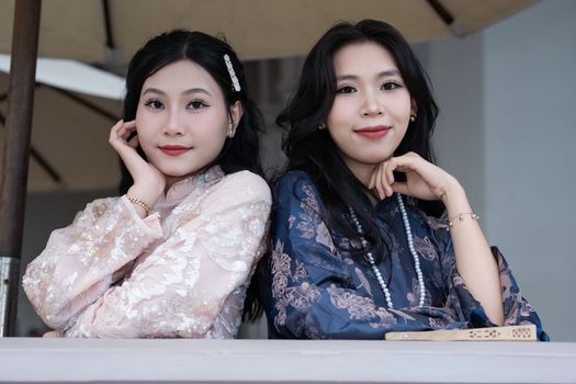 Two women in elegant traditional attire pose gracefully with a neutral backdrop.