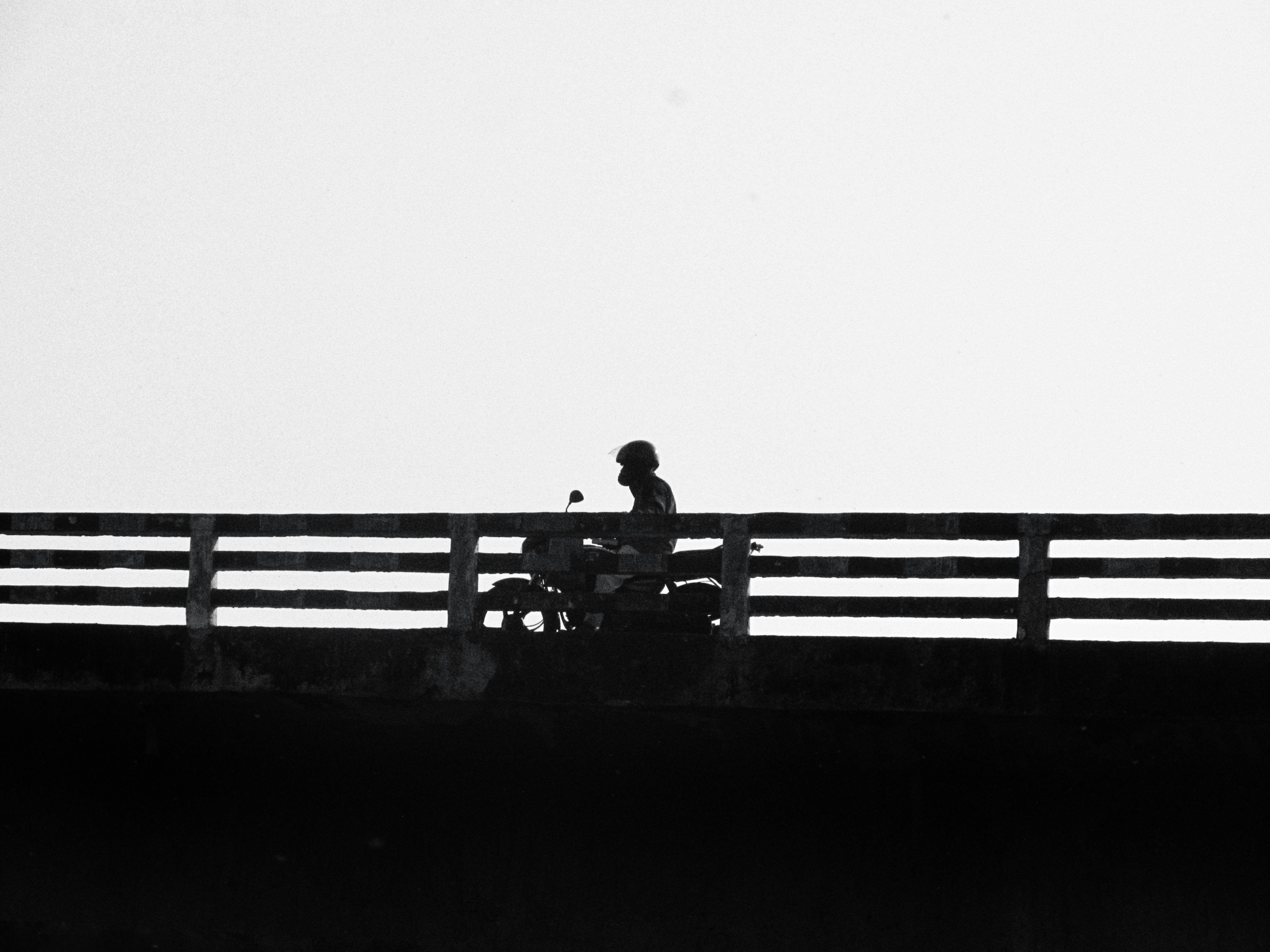 Gratis Silueta de un motociclista en un puente contra un cielo despejado en blanco y negro. Foto de stock