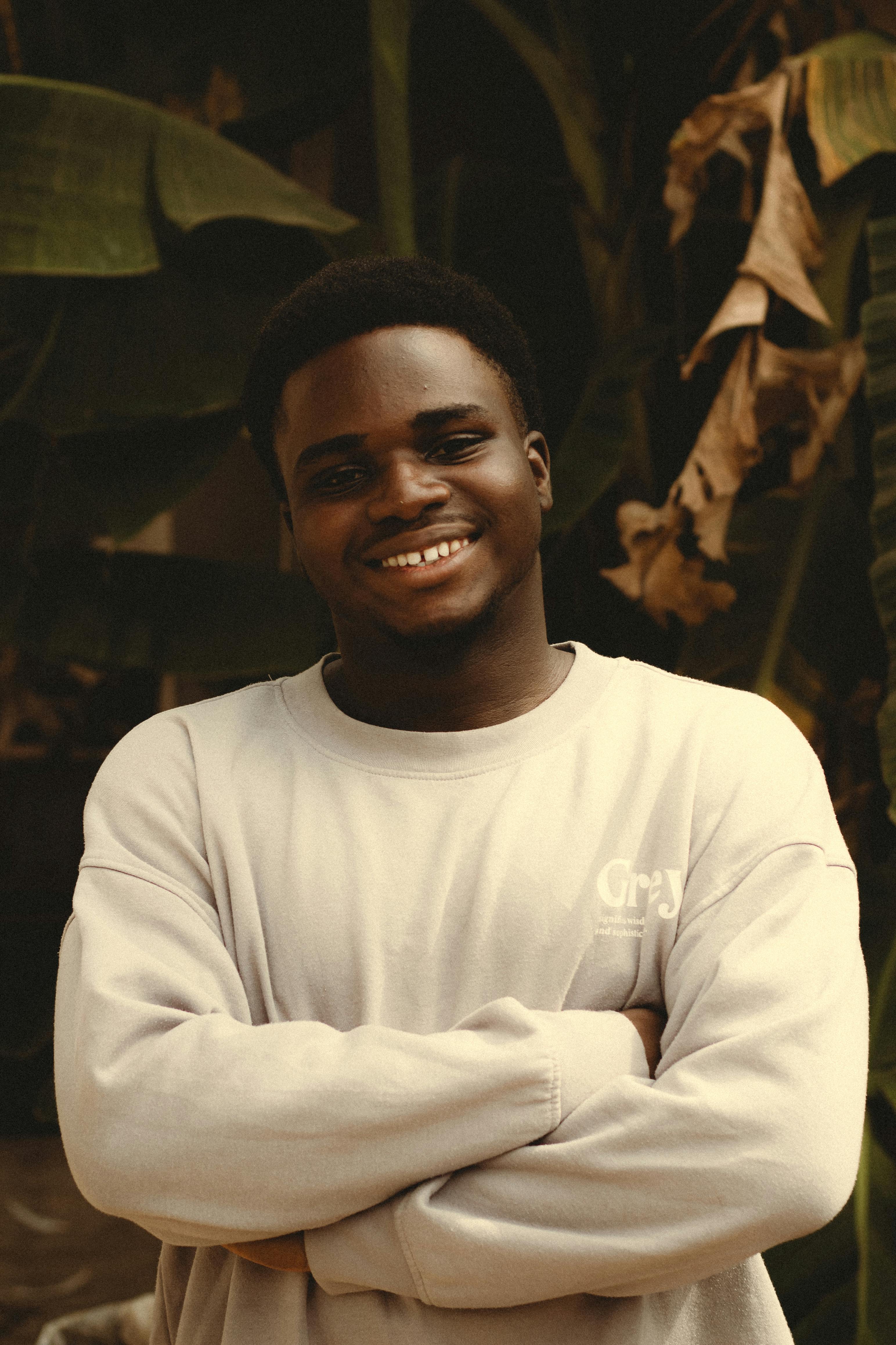 Casual portrait of a young man smiling confidently with arms crossed in a natural setting.