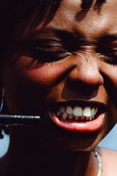 A powerful close-up of a woman applying lipstick with intense expression, captured in natural sunlight.