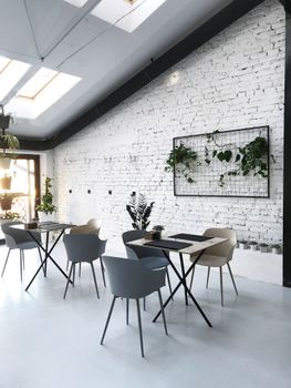 A chic, contemporary cafe interior featuring white brick walls, modern furniture, and decorative indoor plants.