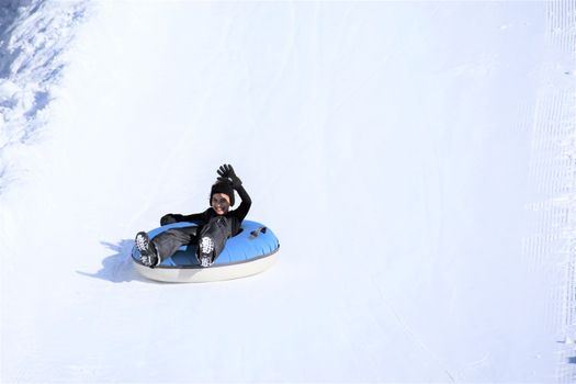 A child snow tubing down a snowy slope, waving and smiling. Fun winter activity.