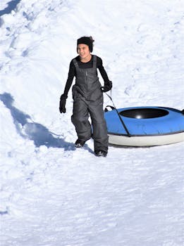 A teenager delightedly snow tubing in a beautiful winter landscape with a blue and white inflatable tube.