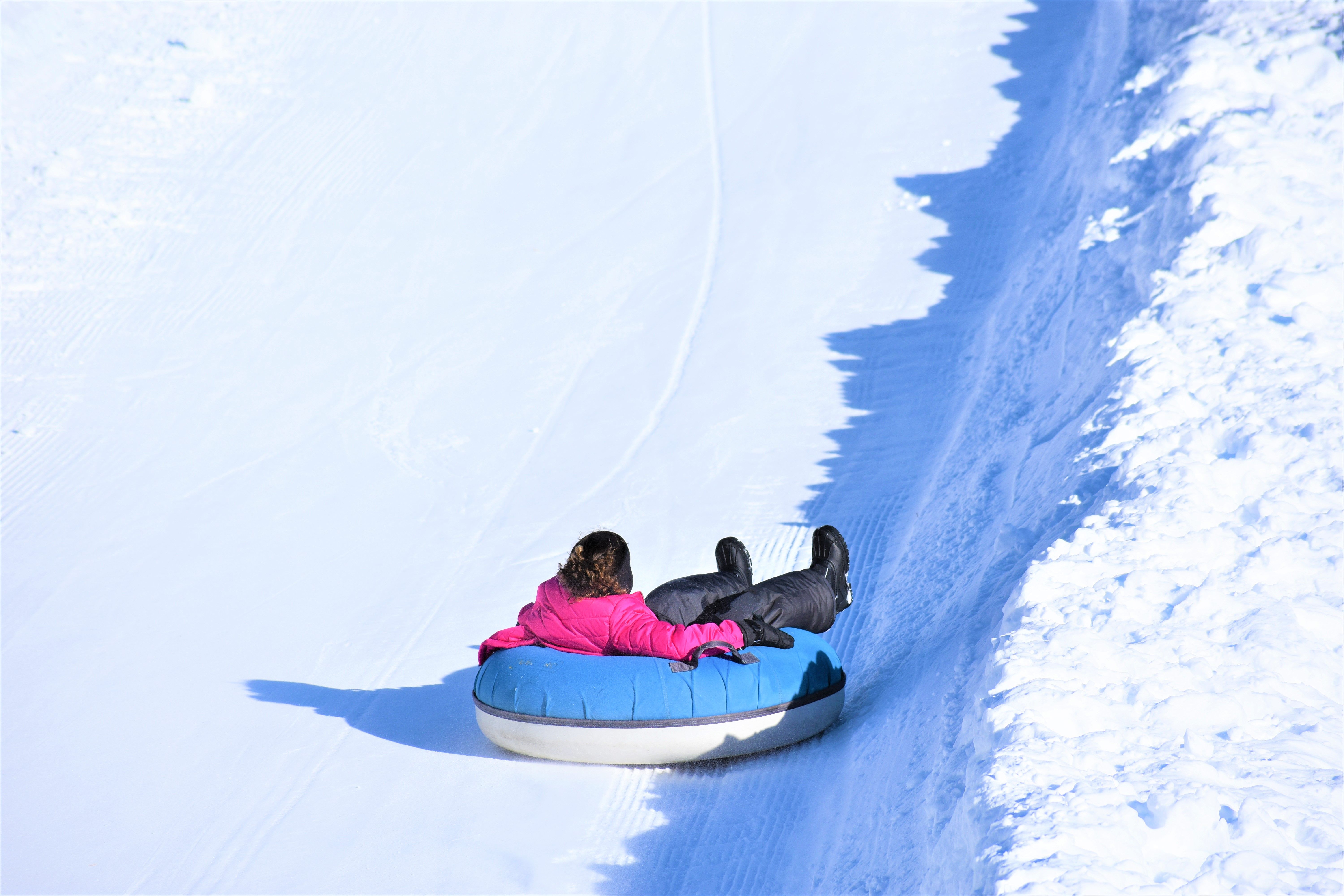A person in bright winter clothing snow tubing down a sunny hill
