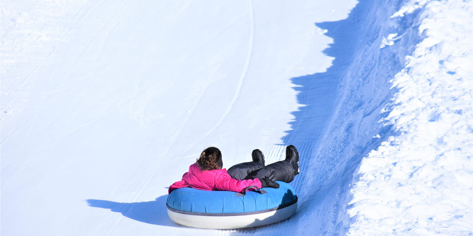 A person in bright winter clothing snow tubing down a sunny hill