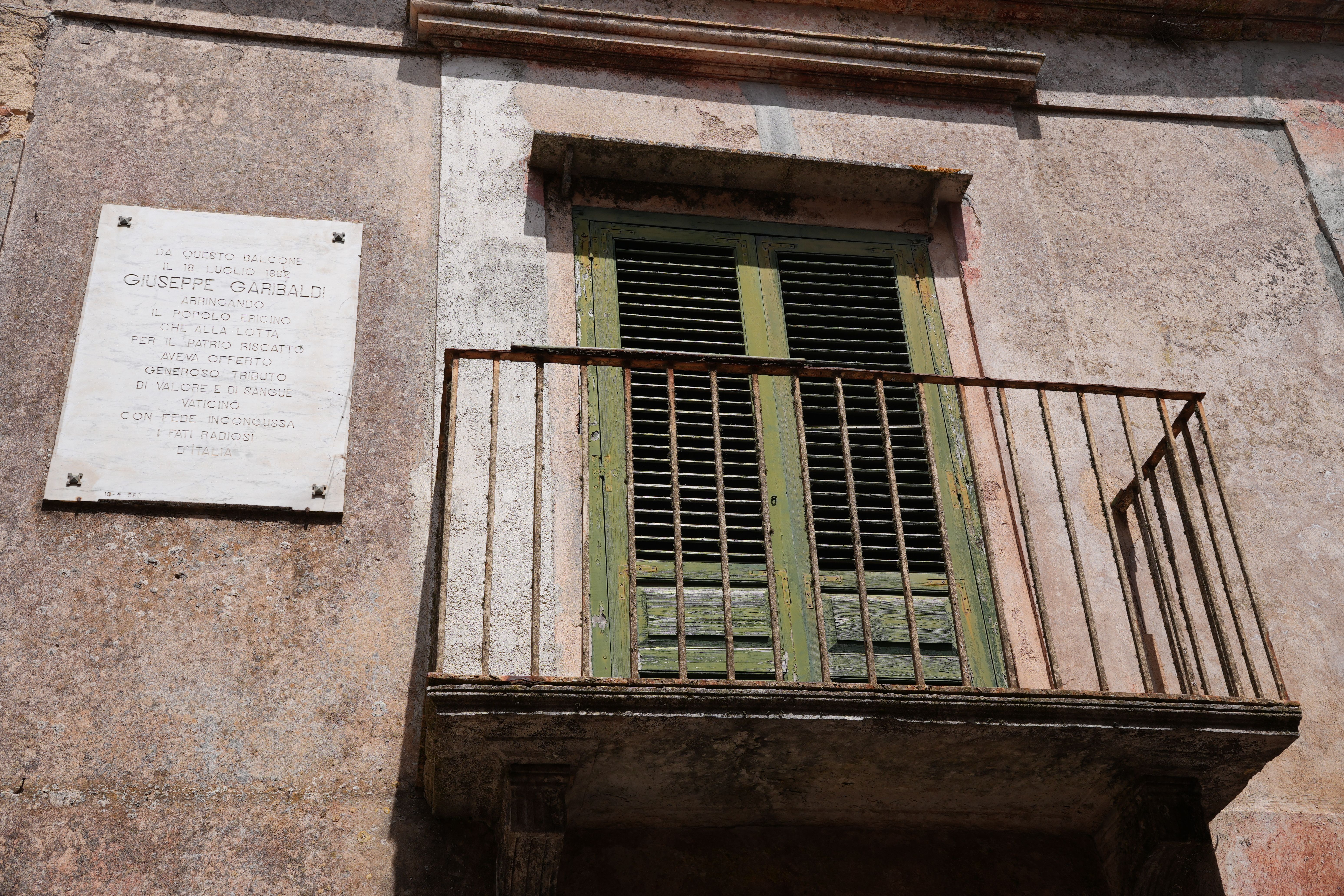 Rustic Italian balcony in Erice, Sicily featuring a Giuseppe Garibaldi plaque.
