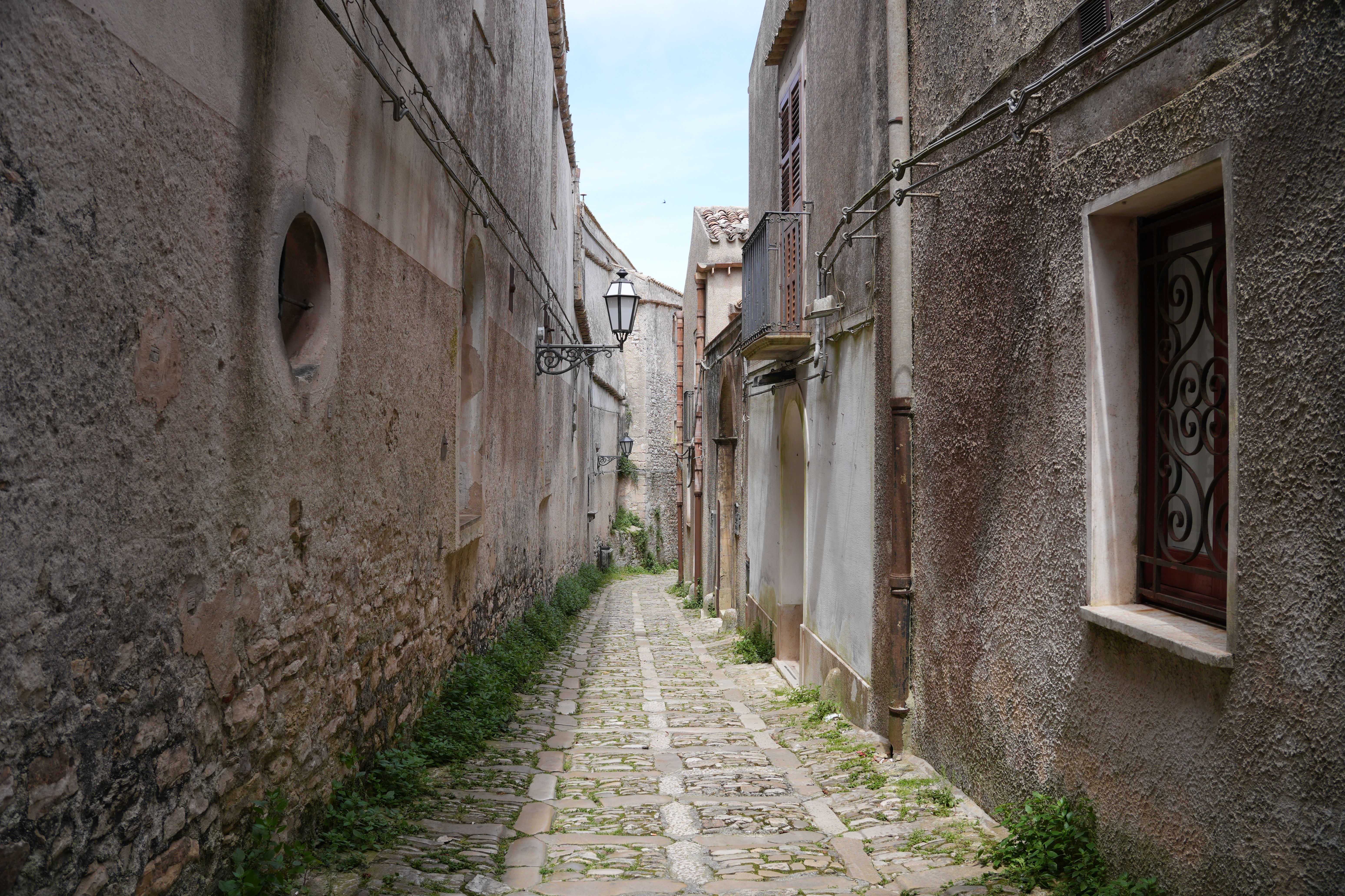 Explore a picturesque narrow street in Erice, Sicily, featuring rustic stone buildings and vintage charm.