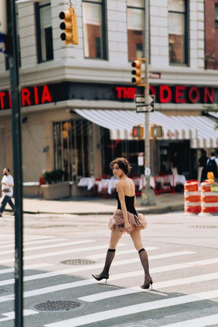 Stylish woman in an elegant dress crossing the street in New York City, showcasing urban fashion.