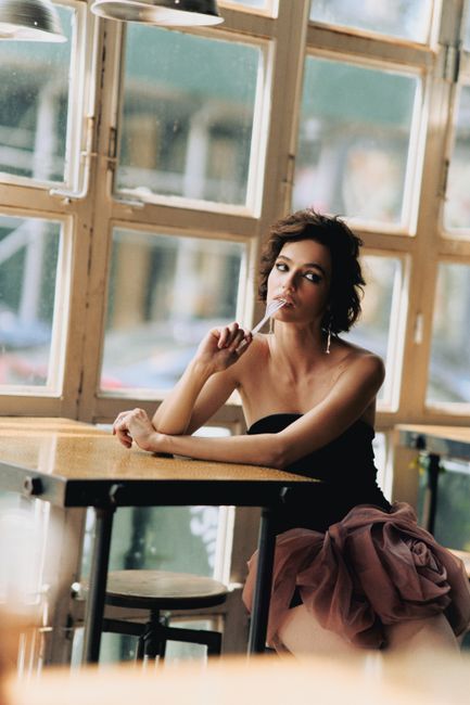 Elegant woman in a chic dress poses thoughtfully by a cafe window in New York City.