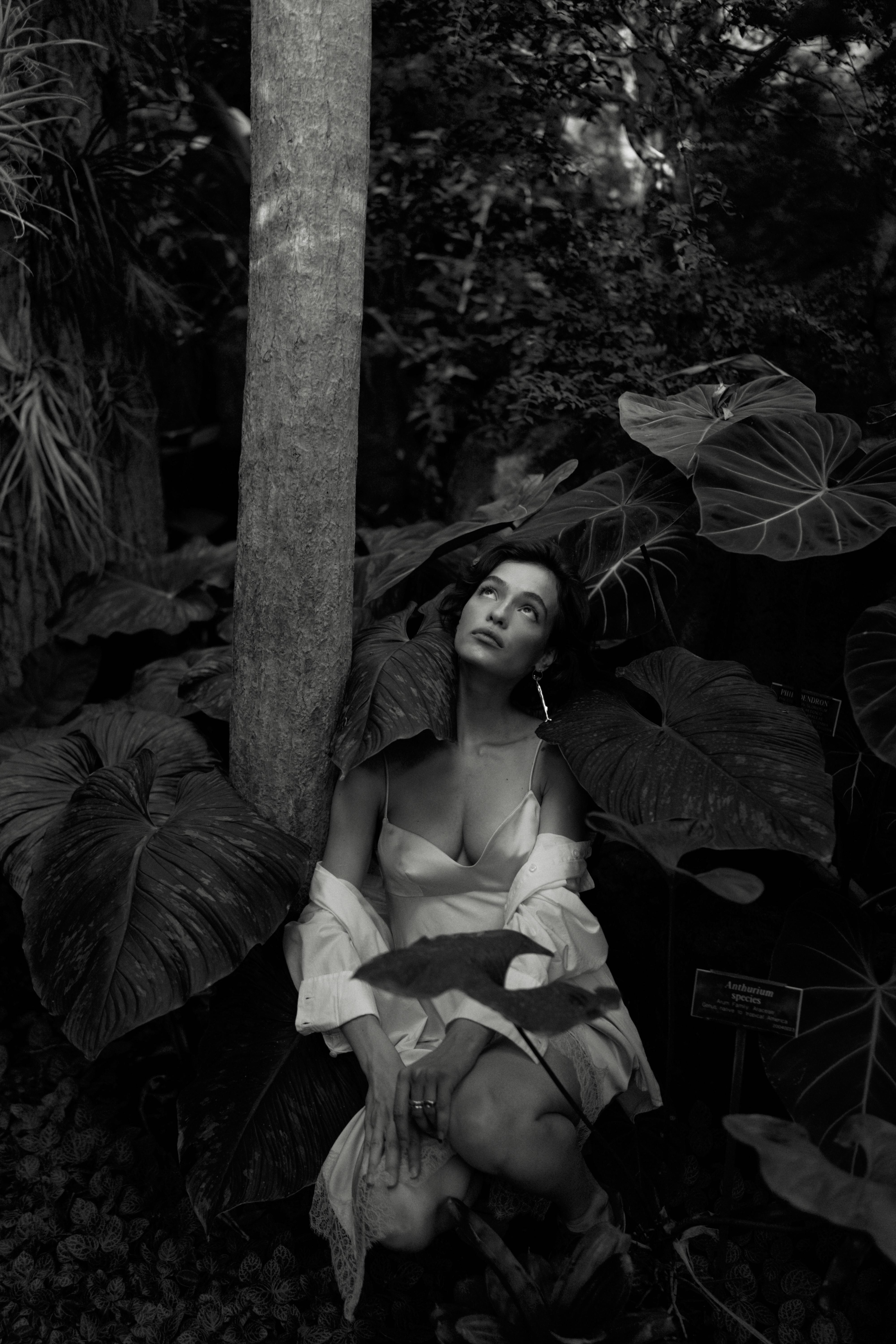 Stylish woman poses among large tropical leaves in a botanic garden, creating an elegant and contemplative mood.