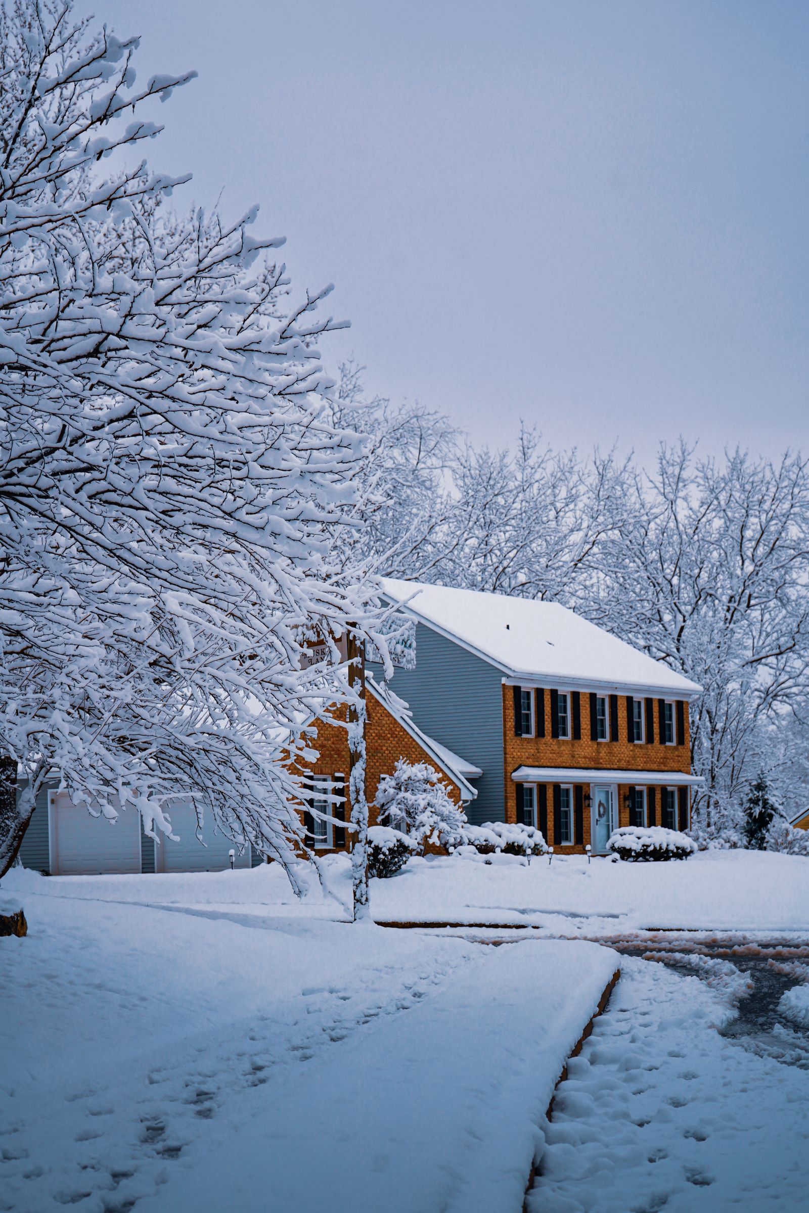 Snow-covered two-story brick and siding home framed by frosted trees on a quiet residential street, Eagle Chase, Naperville IL