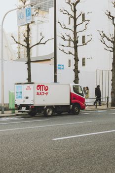 A delivery truck parked on a Tokyo street with winter trees and cityscape background.