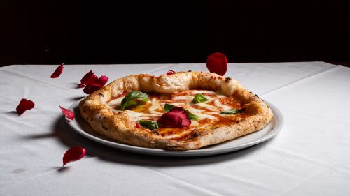 Free A beautifully presented Margherita pizza with fresh basil on a white tablecloth, surrounded by rose petals. Stock Photo
