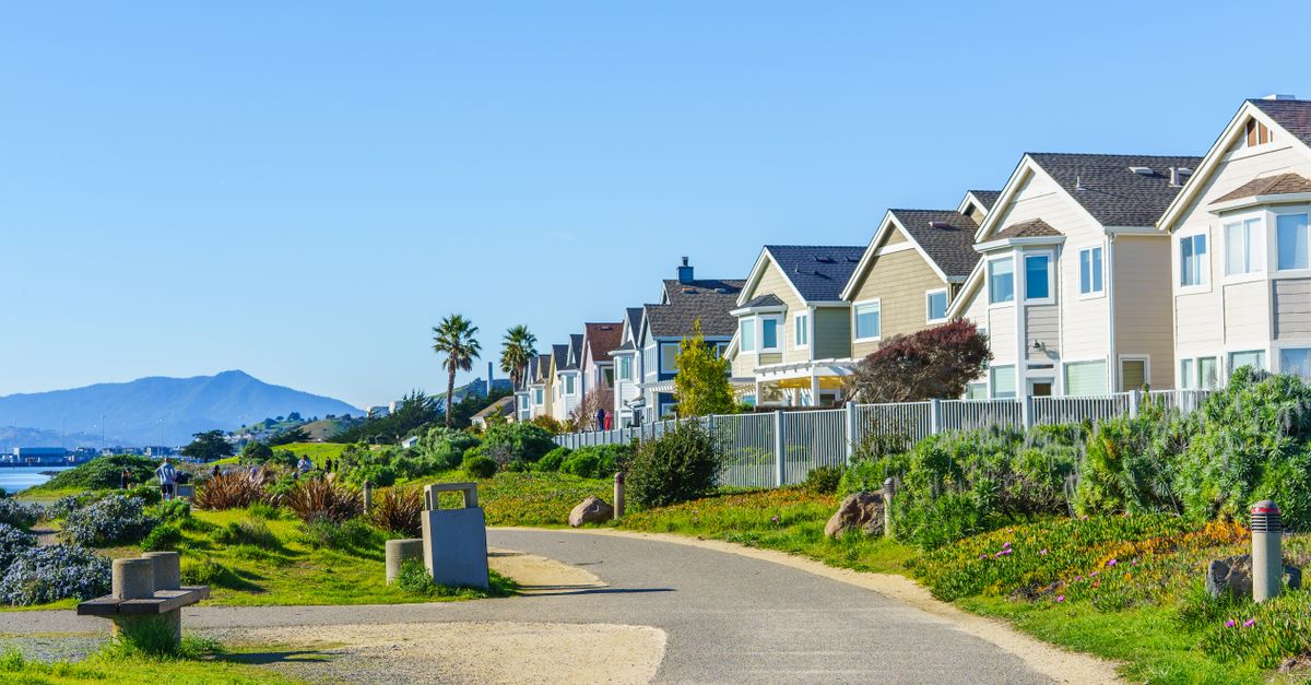 Bright daytime view of a coastal neighborhood with a scenic path and distant mountain backdrop.