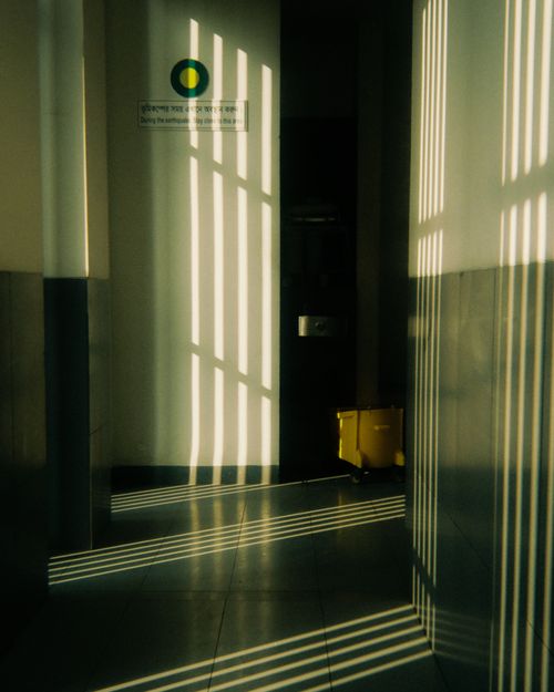 Free Sunlight casting dramatic shadow patterns in an empty hallway with a yellow mop bucket. Stock Photo