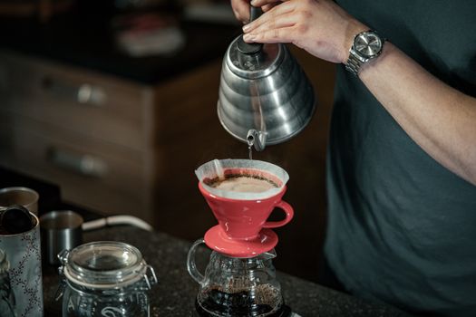 Man preparing pour over coffee with red dripper. Indoor setting, showcasing coffee preparation.