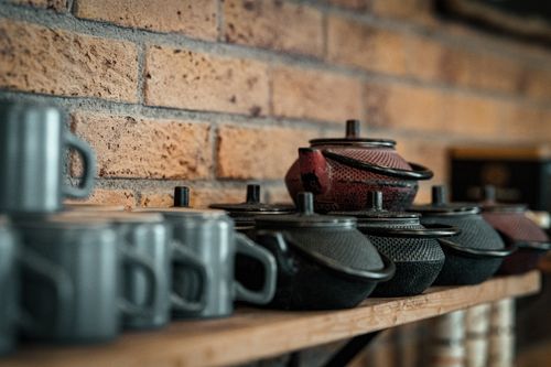 Free Stylish arrangement of teapots and mugs on wooden shelf in a boutique with brick wall backdrop. Stock Photo