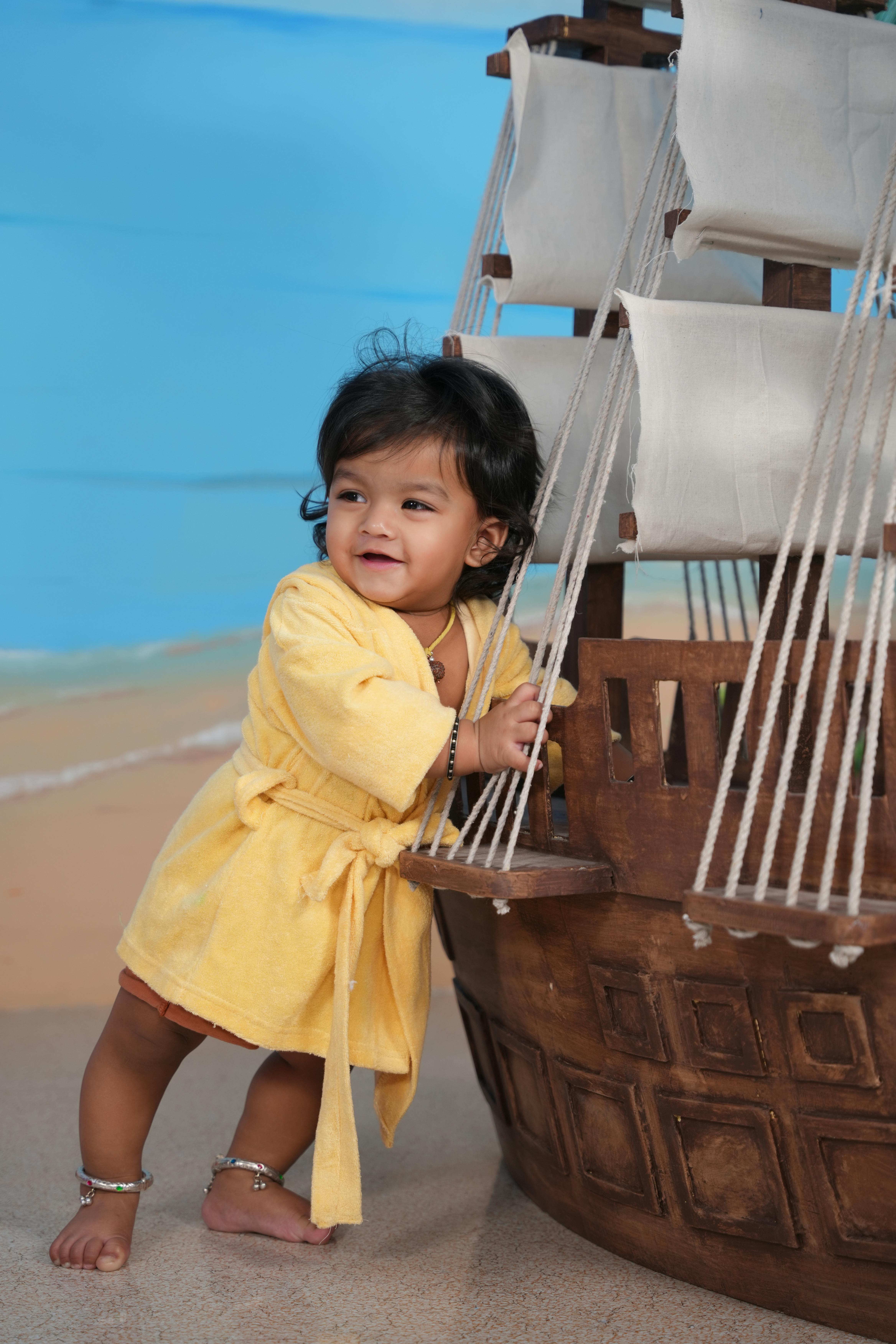 Gratis Bayi menggemaskan berbalut pakaian kuning dengan gembira bermain dengan model kapal di dalam ruangan. Foto Stok