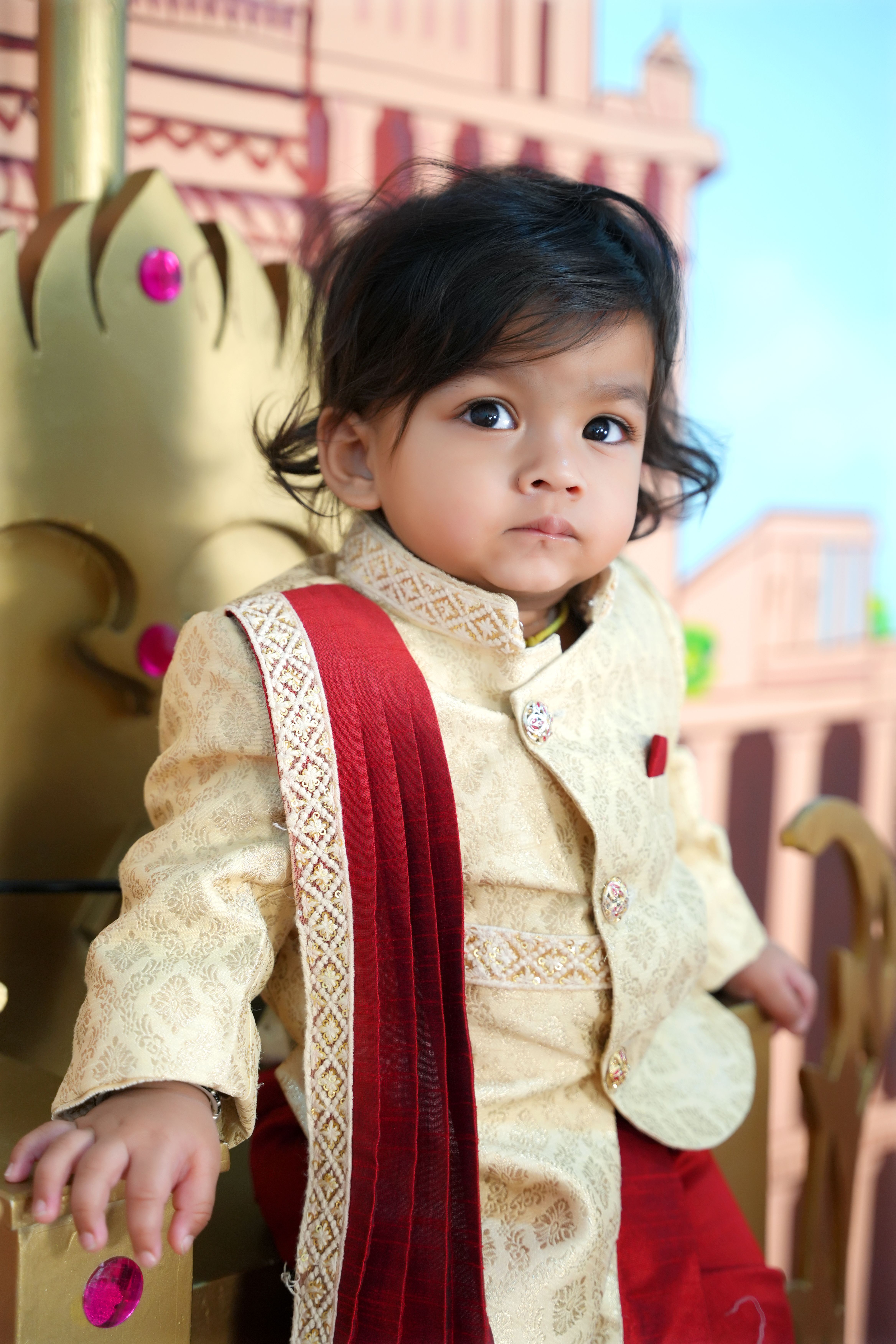 Cute child in traditional Indian outfit sitting on a decorative throne outdoors.