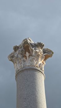 A detailed view of a Corinthian column against a cloudy backdrop, highlighting classical architecture.