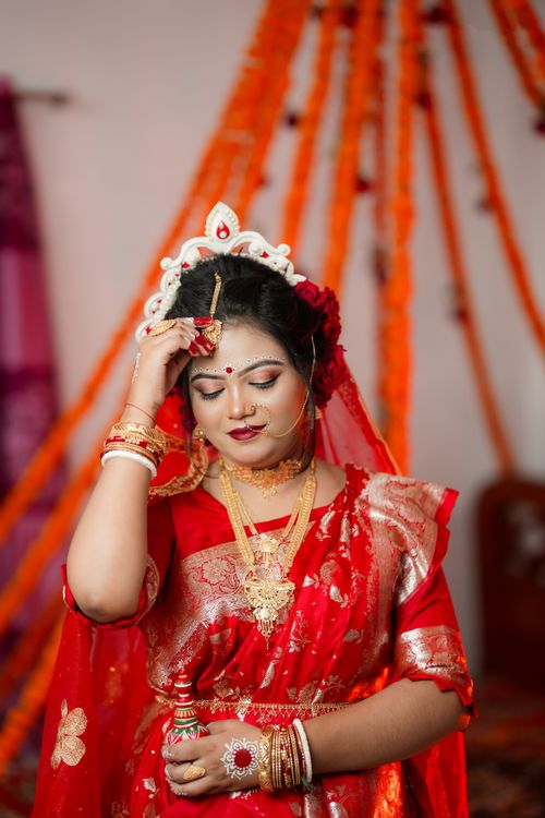Free Beautiful South Asian bride in traditional red saree adorned with gold jewelry and intricate makeup. Stock Photo