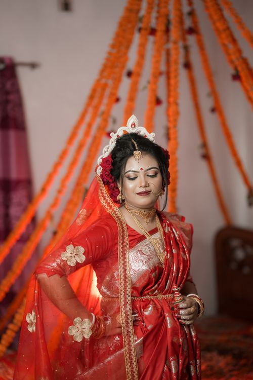 Free Beautiful Bengali bride adorned in red saree and gold jewelry, celebrating her wedding indoors. Stock Photo