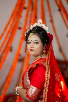 Portrait of a beautiful Bengali bride in traditional red saree and gold jewelry.