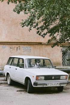 Classic white car parked near a wall with graffiti, creating a nostalgic urban scene.