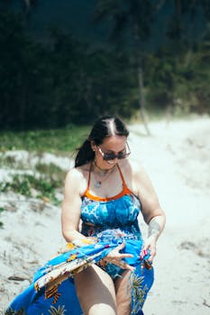 Woman enjoying a sunny day on a tropical beach, wearing blue attire and sunglasses.