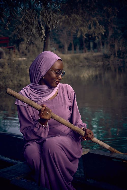 Free A serene image of a woman in lilac attire sitting by a riverside, holding a paddle. Stock Photo